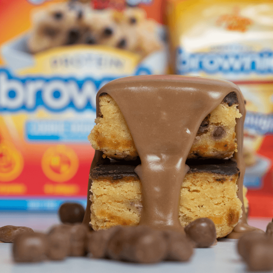 Delicious cookie dough brownie topped with smooth chocolate sauce, showcasing protein-rich treat and packaging.