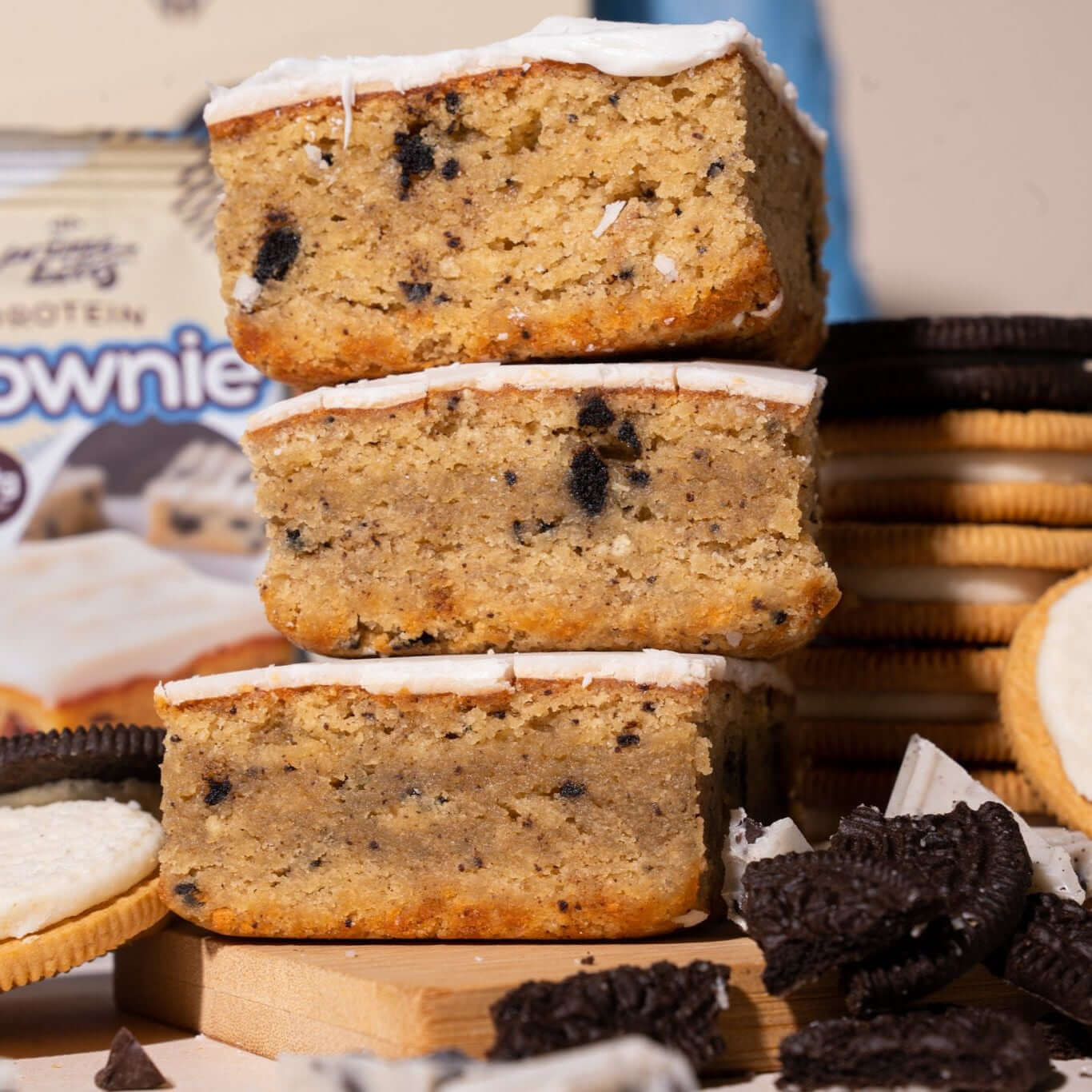 Stack of Cookies & Cream Blondies topped with icing, surrounded by cookies and crumbs, showcasing a nutritious snack.