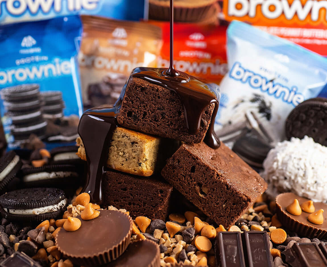 Decadent protein brownies topped with chocolate sauce, surrounded by cookie pieces and assorted toppings.